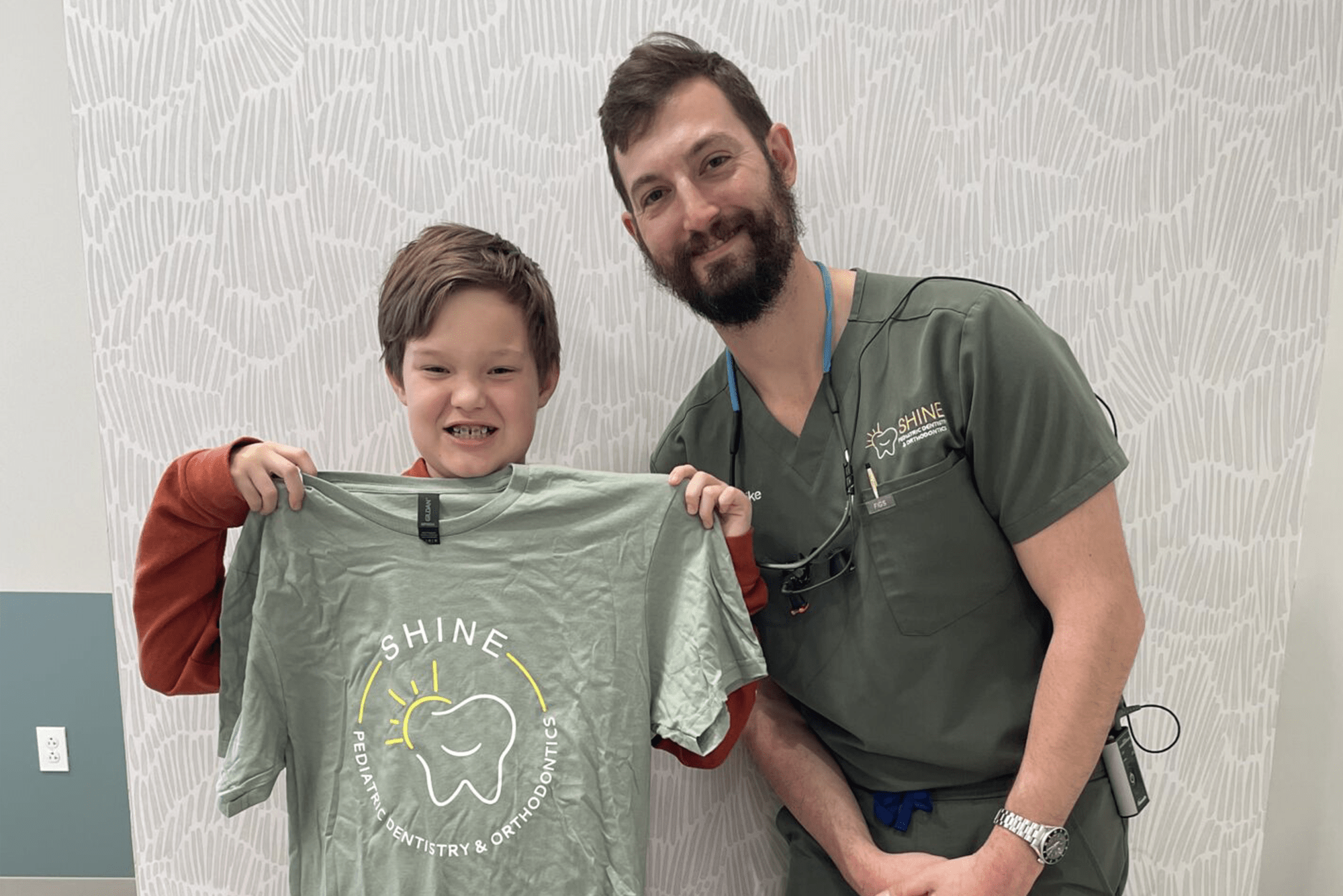 boy smiling, holding tee shirt next to doc